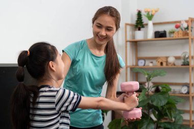 Bir anne, kızına pembe bir dambılı kaldırması için yardım eder, evde destekleyici bir sağIık ortamı sağlar..