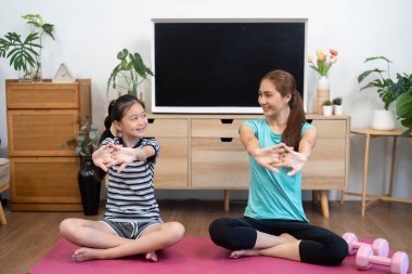Bir anne ve kızı yoga minderinde birlikte uzanıyor. Parlak bir oturma odasında aile bağlarını güçlendiriyor..