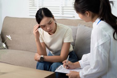 Bir psikolog terapi seansında duygularını ifade eden genç bir kadını dikkatle dinler..