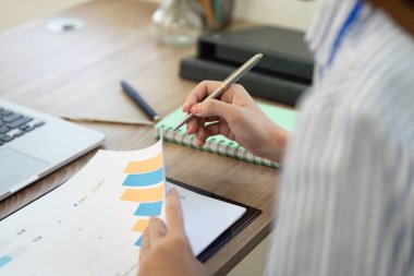 Bir profesyonel, veri eğilimlerini grafiklerle analiz eder, ev ofis ortamında analitik becerileri vurgular.