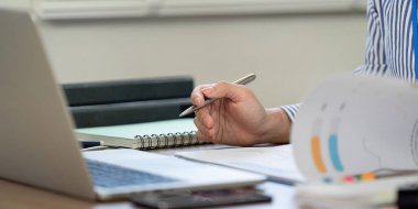 Odaklanmış bir birey, bir kalemle notlar yazar, bir ev ofisi ortamında önemli bilgiler yakalar..