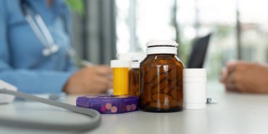 Bir dizi ilaç şişesi, hasta bakımındaki sağlık ve sağlığın önemini vurgulamak üzere doktor masasında sergilenmektedir..