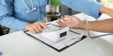 Bir sağlık uzmanı konsültasyon sırasında hastaların kan basıncını ölçer, klinik ortamdaki sağlık ve sağlığın önemini vurgular.