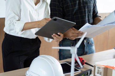 Mühendisler sürdürülebilir enerji projeleri, yenilenebilir teknolojiye odaklı modern çalışma alanındaki planlar ve modelleri gözden geçirirler..