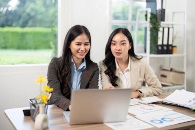 İki iş kadını bir dizüstü bilgisayarda iş birliği yapıp verileri analiz ediyor, parlak bir ofis ortamında görüşleri tartışıyorlar..