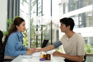 Bir hemşire, erkek bir hastayla ilgilenir ve parlak bir sağlık ortamında tedavi planını ve ilaçlarını tartışır..