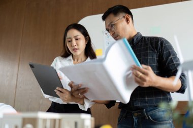 Sürdürülebilir tasarım stratejileri üzerinde işbirliği yapan mühendisler, modern bir çalışma alanındaki planlar ve modelleri gözden geçiriyorlar..