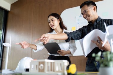 Mühendisler sürdürülebilir mimari planlarını tartışırken modern bir ofiste modelleri ve planları gözden geçiriyorlar..