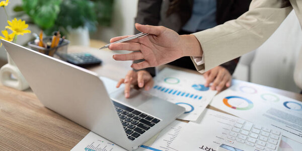 Businesswomen collaborating on a laptop, discussing financial reports and data visualizations in a modern office environment.
