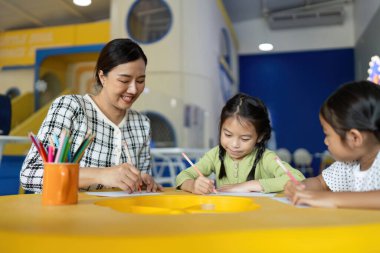 Bir öğretmen genç öğrencilere yaratıcı bir aktivitede rehberlik eder, okula dönüş sezonunda öğrenmeyi teşvik eder..