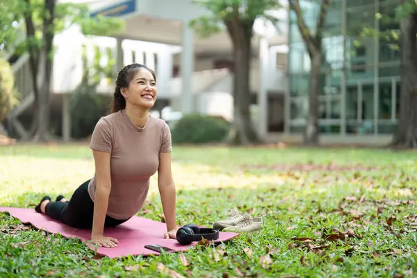 Bir kadın, sakin bir parkta yoga seansından zevk alır. Dikkatli bir egzersiz yaparak rahatlama ve neşeyi teşvik eder..
