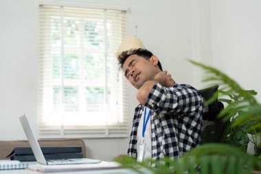 Genç bir profesyonel dizüstü bilgisayarın başında oturmuş, uzaktan çalışma ortamlarında ergonomik sağlığın önemini vurguluyor..