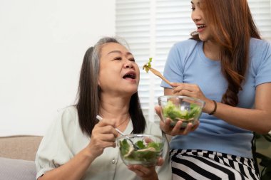 Bir kız, annesine taze salata yedirir, besleyici bir ilişki ve sağlıklı beslenmeye olan bağlılığını gösterir..