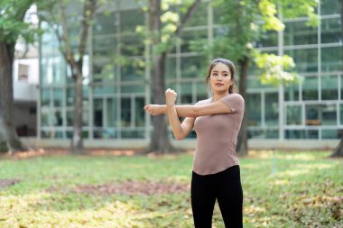 Bir kadın parkta kollarını uzatır, sağlığını artırır ve doğal bir çevrede fiziksel sağlığını destekler..