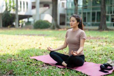Bir kadın sakin bir parkta meditasyon yapıyor, nefesine odaklanıyor ve zihinsel sağlığını ve farkındalığını arttırıyor..