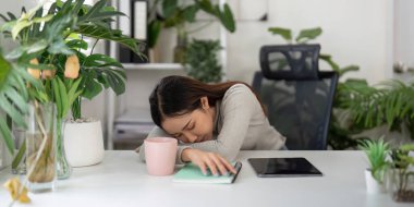 Masasında yatan bir kadın, iş yerindeki yorgunluğu ve modern ofis ortamında mola verme ihtiyacını gösteriyor..