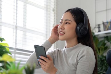 Parlak bir ofis ortamında akıllı telefonuyla müzik dinlerken kulaklık takan ve gülümseyen bir kadın..