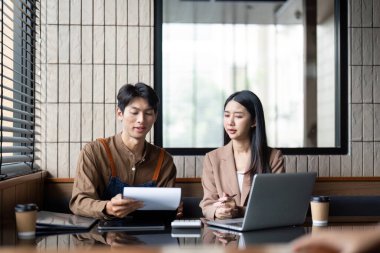 Bir kadın ve bir erkek proje detaylarını tartışıyor, belgeleri analiz ediyor ve şık bir çalışma alanında fikirleri paylaşıyor..