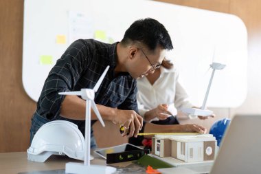 İki mühendis birlikte sürdürülebilir bir proje üzerinde çalışıyorlar, modern bir çalışma alanında çevre dostu tasarımlar ve rüzgar enerjisi çözümleri tartışıyorlar..