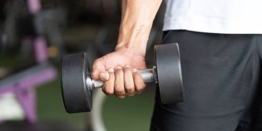 Kas yığını bir dambılı kavrıyor. Güç gösterisi yapıyor. Spor salonunda forma girmeye kendini adamış..