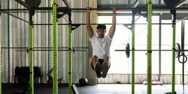Kararlı genç bir adam spor salonu halkaları üzerinde kas egzersizi yapıyor. Modern bir spor salonunda güç ve atletizm gösterisi yapıyor..