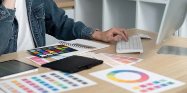 Bir profesyonel, parlak ve düzenli bir çalışma alanında klavye ve çeşitli örnekler kullanarak renk koordinasyonuna girer.