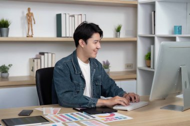 Genç bir tasarımcı, parlak bir ortamda dijital tasarıma modern bir yaklaşımı yansıtan renk paletleriyle çevrili bir bilgisayarda yazı yazar..