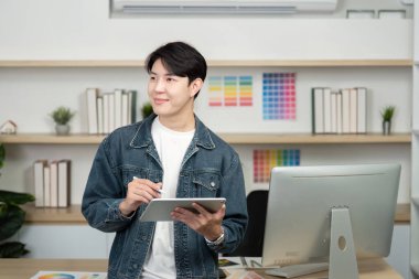 Gülümseyen bir tasarımcı, parlak bir çalışma alanında yaratıcılık ve modern tasarım tekniklerini gösteren renk seçeneklerini keşfetmek için bir tablet kullanır..