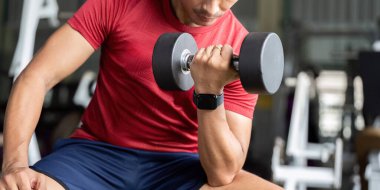 Odaklanmış bir adam spor salonunda bir dambılla güç antrenmanına başlar, sağlık ve zindeliği teşvik eder..