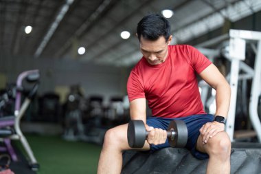 Odaklanmış bir adam spor salonunda bir dambılla güç antrenmanı yapar, egzersiz yaparak sağlığını ve zindeliğini arttırır..