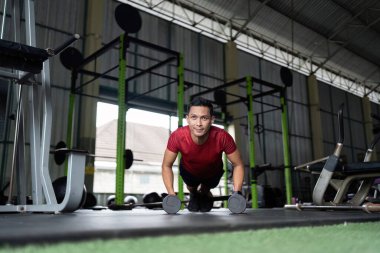 Kararlı bir adam dambıl kullanarak şınav çeker, spor salonunda vücut kuvveti eğitimine odaklanır..