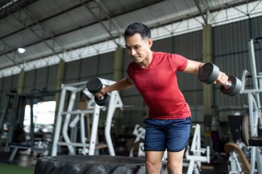 Formda bir adam halterlerle yan yana yükselir, spor salonundaki vücut gücü eğitimine odaklanır..