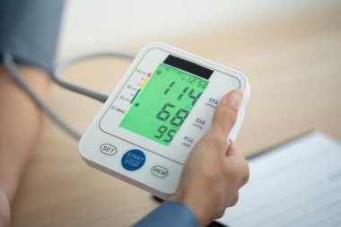 Bir sağlık uzmanı, dijital tansiyon monitörünün sonuçlarını göstererek hastanın anlayışını ve bakımını sağlar..