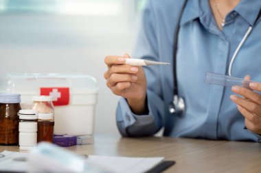 Bir sağlık uzmanı termometre ve ilaç kullanarak hastaların sağlığını değerlendirir, sağlık ve bakımı vurgular.