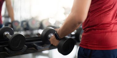 Bir adamın dambılı kavradığı yakın çekim, spor salonundaki dayanıklılık eğitimini ve zindeliği vurguluyor..