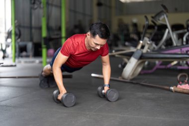 Kararlı bir adam spor salonunda dambıllarıyla şınav çeker. Gelişmiş sağlık için güç gösterisi yapar..