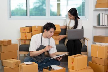 Bir çift hevesle paketleri hazırlıyor ve lojistik planlıyorlar, parlak bir çalışma alanında takım çalışması sergiliyorlar..