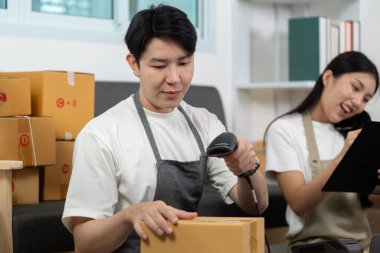 Bir çift birlikte çalışıyor, envanter ve paketleri yönetmek için barkod tarayıcısı kullanıyor, takım çalışmasını ve lojistikteki verimliliği vurguluyor..