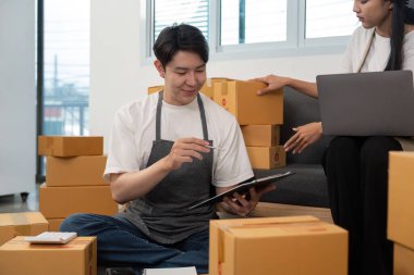 Bir çift ortak çalışma alanında birlikte oturur, lojistiği analiz eder ve paketleri yönetir, işbirlikçi çabalarını vurgular.