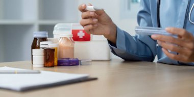 Bir sağlık hizmeti sağlayıcısı, elinde termometre ve ilaç bulunduran bir konsültasyon için hazırlanır. Hasta sağlığı ve ilaç yönetimi üzerine yoğunlaş.