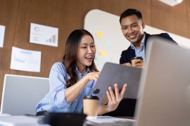 Bir iş ekibi modern bir ofiste dijital tablet üzerinde coşkuyla işbirliği yaparak takım çalışmasını ve yenilikleri yansıtır..