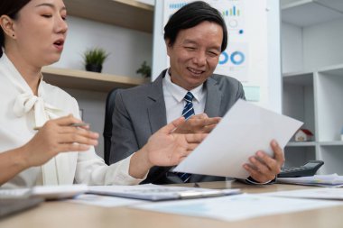 Finansal belge ve grafikleri analiz eden iki iş adamı, şirket ortamında takım çalışması ve stratejik planlama sergiliyorlar..