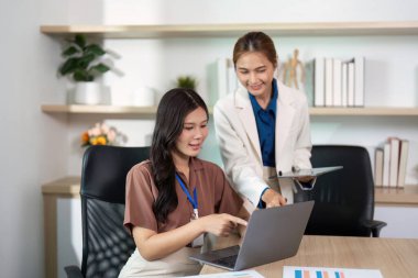 Modern bir ofiste takım çalışmalarını vurgulayan, dizüstü bilgisayarla çalışan ve proje detaylarını tartışan kadınlar.