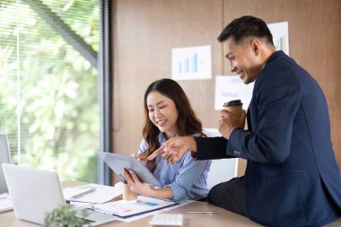 İki profesyonel, takım çalışması ve işbirliğini vurgulayarak, parlak bir ofiste bir tablet üzerinde proje verilerini tartışıyor.