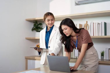 Bir dizüstü bilgisayar ve tablet üzerinde dinamik bir şekilde işbirliği yapan iki kadın, profesyonel ofis ortamında takım çalışması ve yenilik sergiliyor.