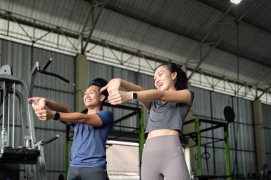 İki arkadaş spor salonunda esneme egzersizi yapıyor, takım çalışmasını vurguluyor ve spor yapmaya kararlı..