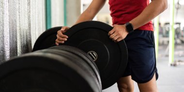 Bir erkek spor salonunda ağırlık ayarlayarak antrenman yapmaya hazırlanır. Güç antrenmanı ve formdan bahseder..