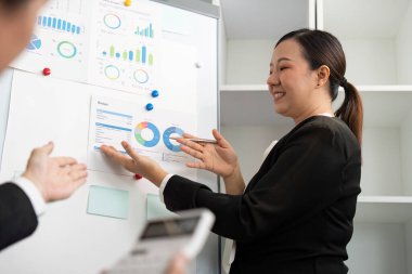 Meslektaşlarına bütçe verilerini hevesle sunan bir kadın, takım çalışması ve stratejik planlamayı vurguluyor.