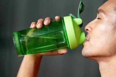 Yeşil karıştırıcı şişeden ferahlatıcı bir yudum alan bir adam, egzersizler sırasında susuzluğun önemini vurgular..