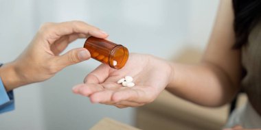 Bir sağlık görevlisi, reçeteli ilaç kutusundan hasta eline ilaç dağıtır, bu da kişisel bakım ve ilgiyi gösterir..